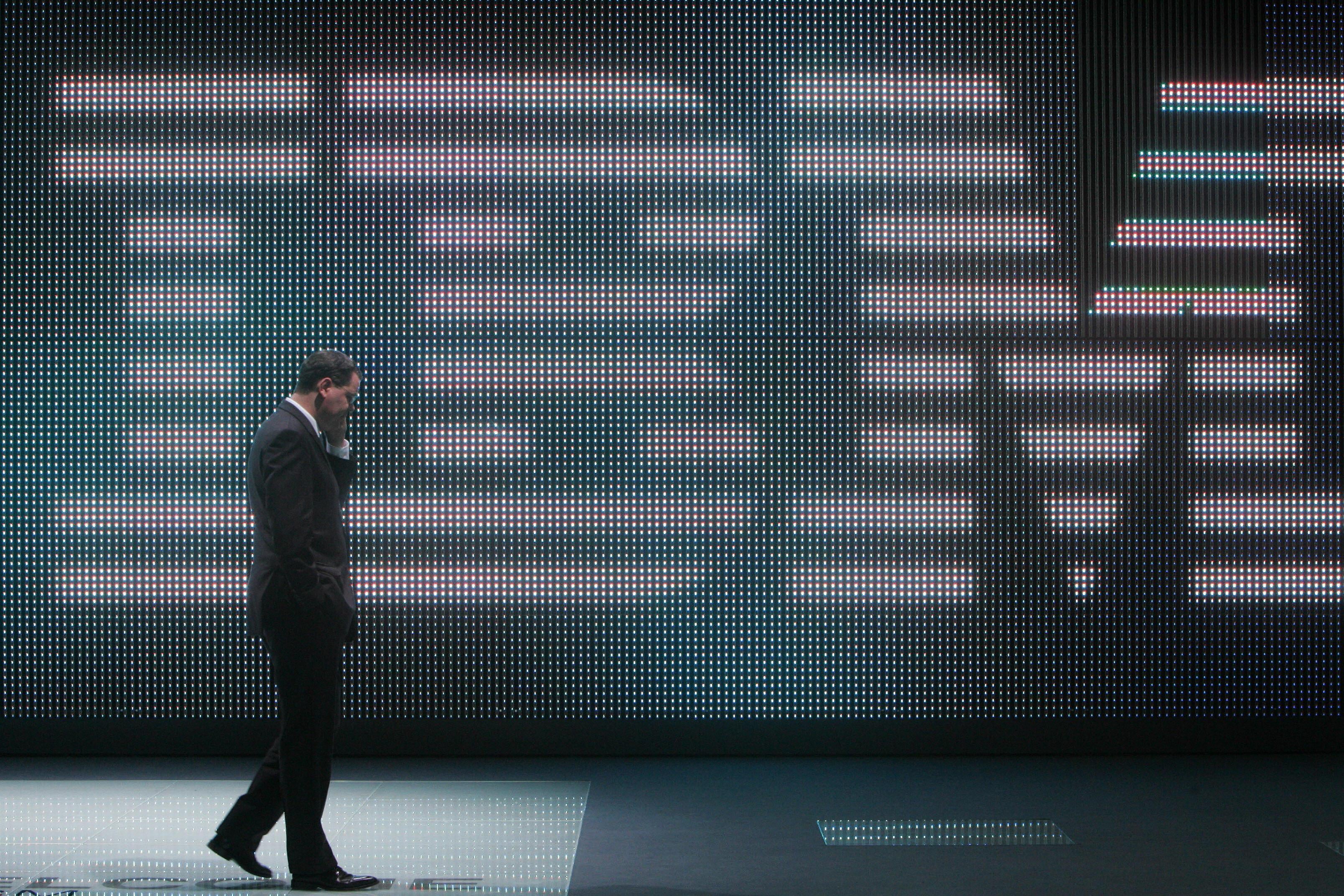 A man talks on his cellphone while walking in front of a giant IBM logo