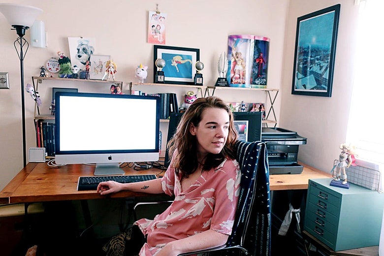 A person sitting in front of a computer that is surrounded by lots of toys and tchotchkes.