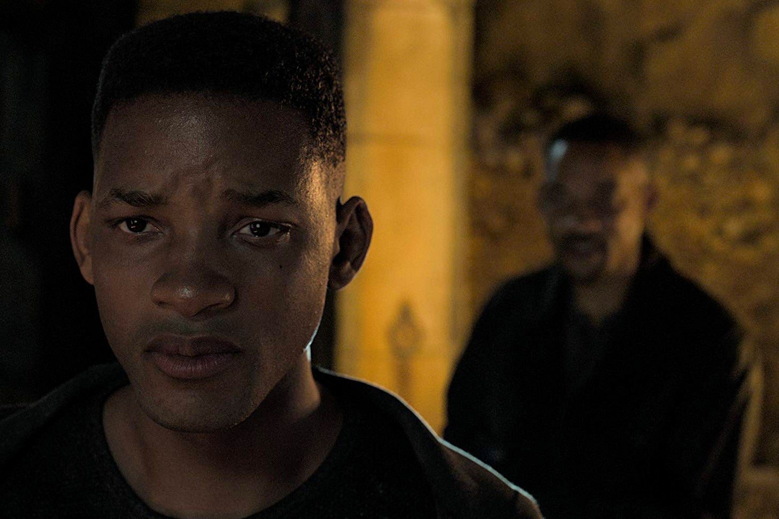 Young Will Smith frowns in the foreground as older Will Smith stands behind him.