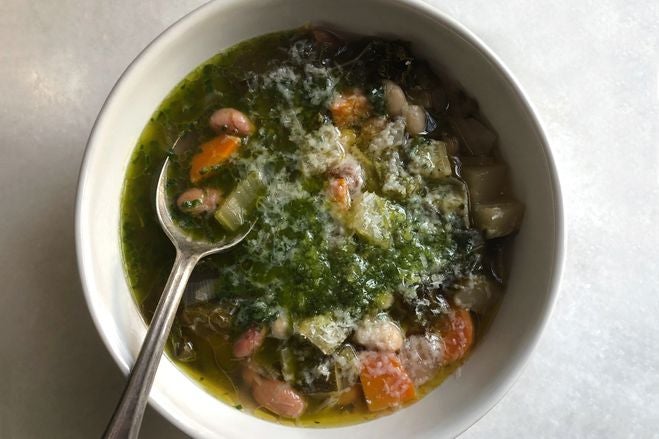 A greenish soup in a bowl with chunks of orange and a silver spoon sticking out.