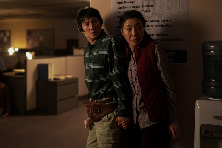 A man in a striped shirt holds his wife's hand in a dark office.