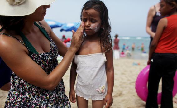 BAT YAM, ISRAEL - AUGUST 02: (ISRAEL OUT) A  woman rubs sunscreen on a child at a beach in Bat Yam, Israel. 