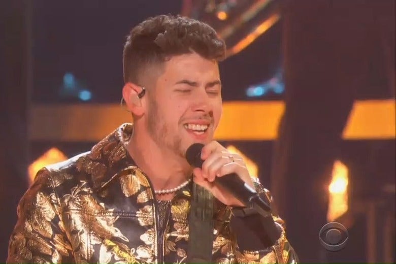 Nick Jonas sings intensely into a microphone at the Grammys, but a piece of food is stuck in his teeth.