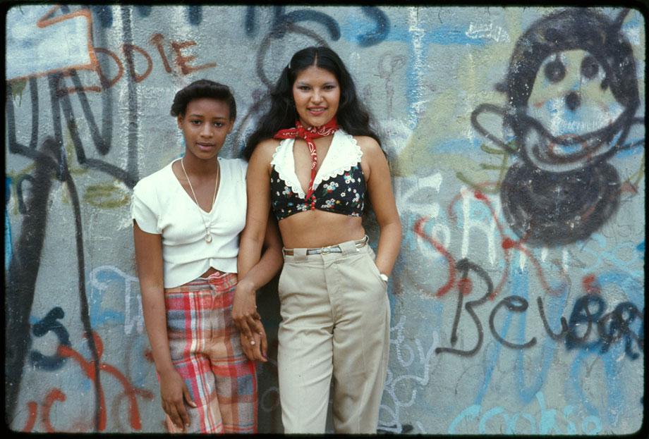 Two Latin girls pose in front of a wall of graffiti in Lynch Park in Brooklyn, New York City. This project is a portrait of the inner city environment. It contains life, great murals on the walls of buildings and people enjoying themselves. Today’s inner city is a contradiction to main stream America’s gas station expressways shopping centers and tract homes. Blacks, latins and poor whites live there.” Danny Lyon, Brooklyn, New York, June 1974