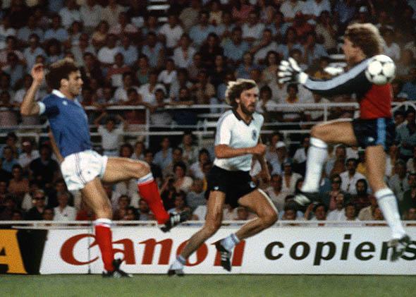 West German goalkeeper Harald Schumacher (R) jumps past the ball as he gets ready to collide with French defender Patrick Battiston during the World Cup.