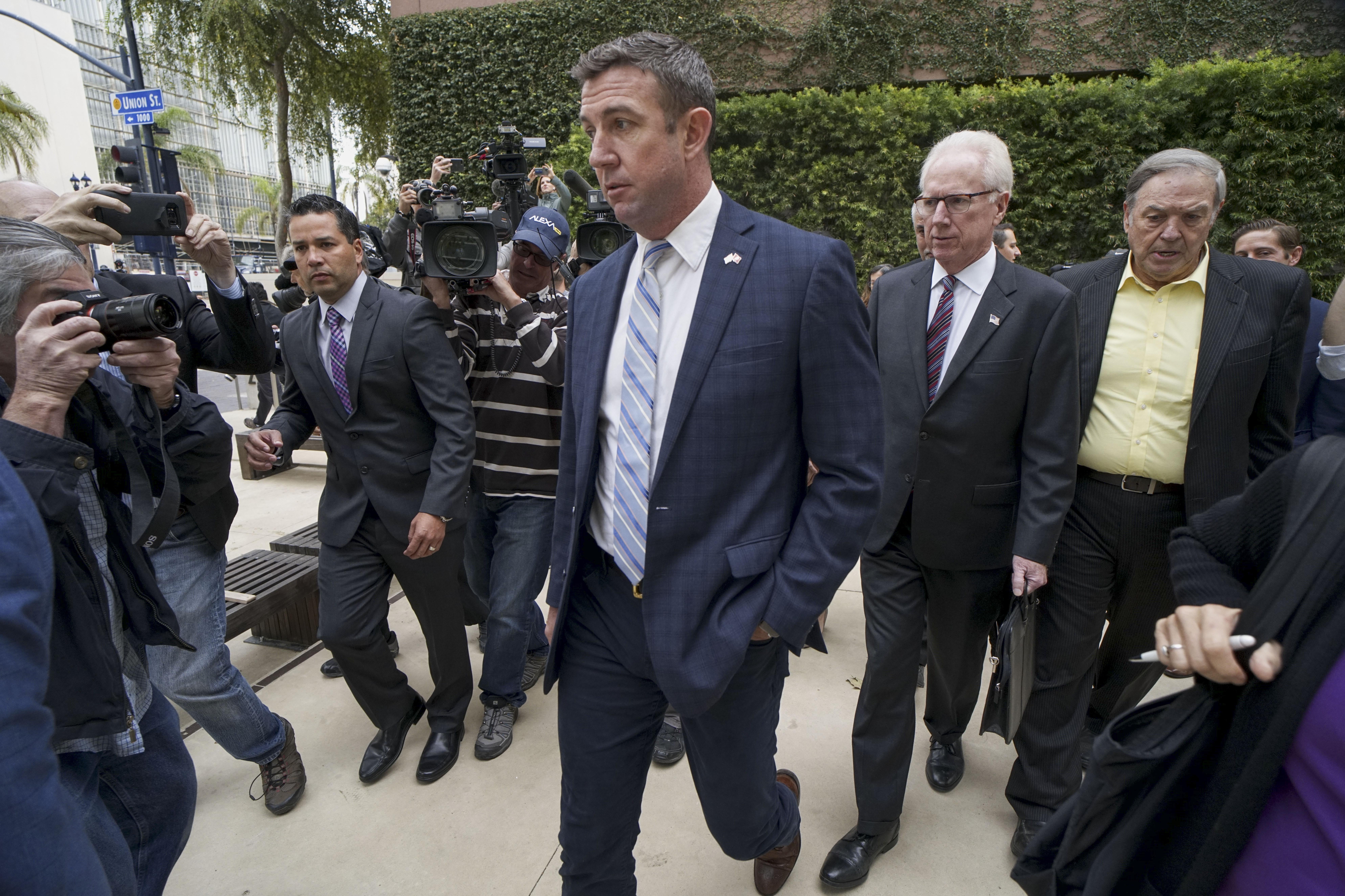 Duncan Hunter walking outside, surrounded by men in suits and photographers.