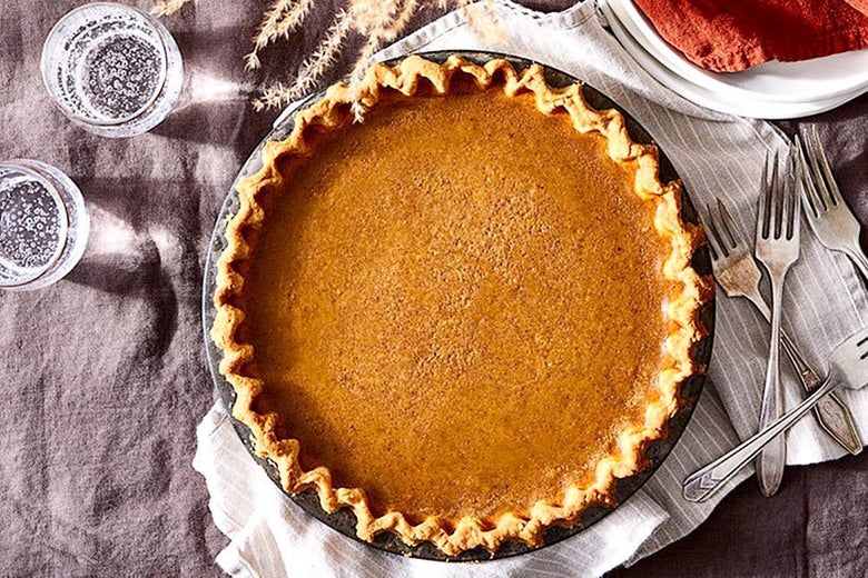 Pumpkin pie set on a tablecloth with forks and glasses of sparkling water beside it