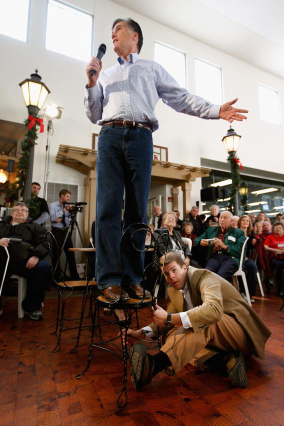Mitt Romney stands in a chair as campaign staff member Garrett Jackson holds it steady