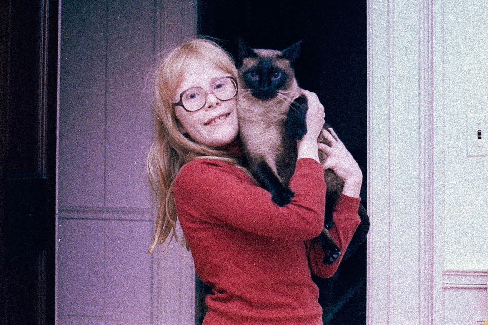 Amy Carter, in a red shirt and glasses, holding her Siamese cat in the White House.