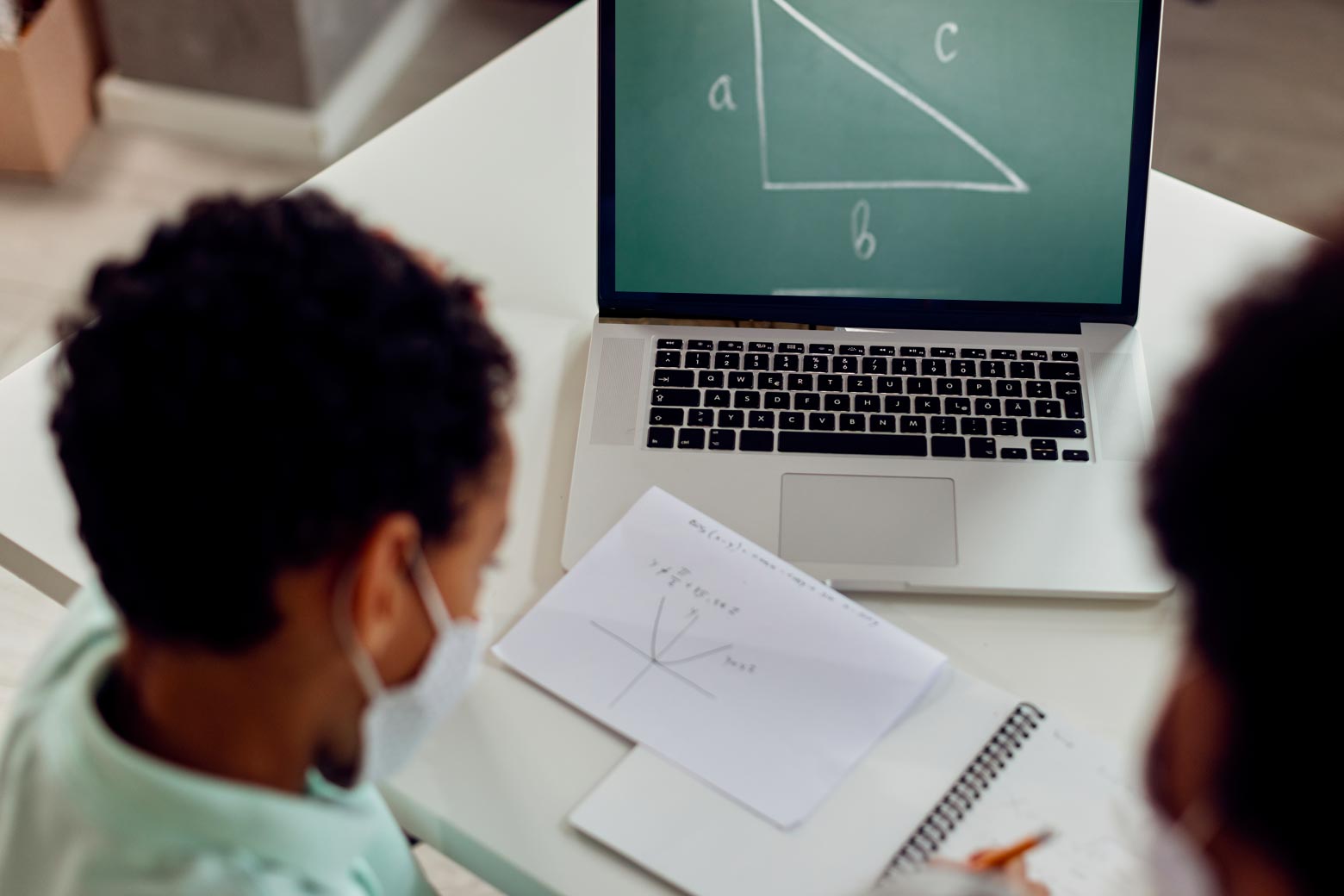 Two kids doing schoolwork in front of a laptop whose screen is displaying a triangle with sides labeled a, b, and c