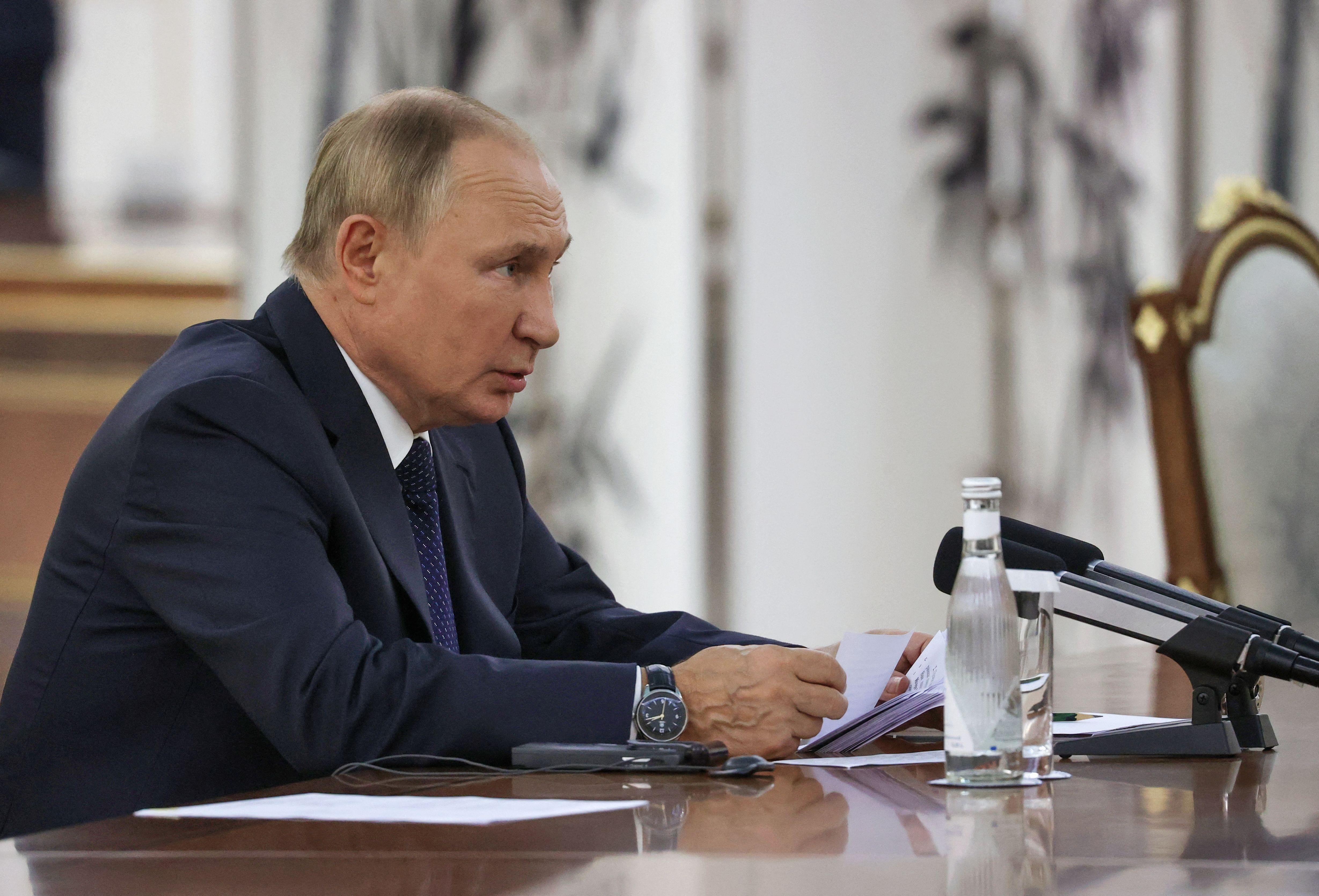 Putin sits hunched with an opened bottle of bottled water in front of him.