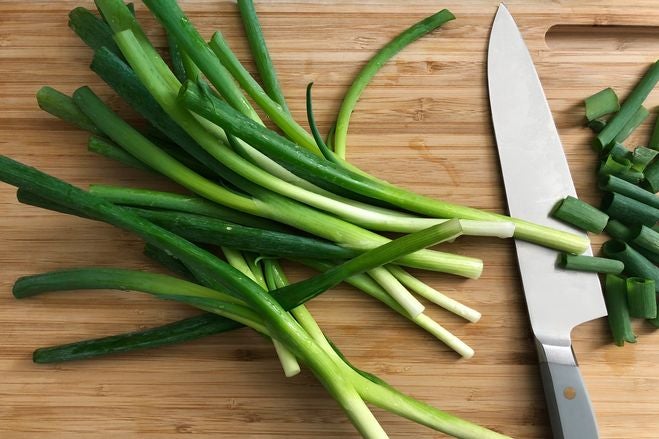 Chopped scallions next to a knife on a cutting board.