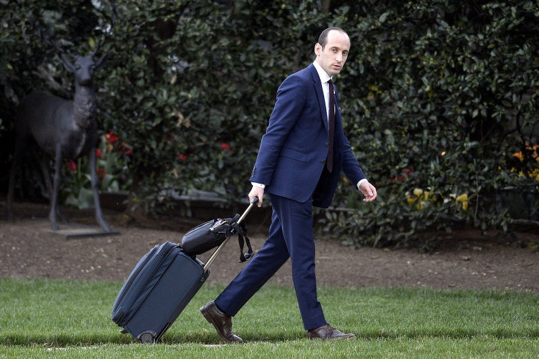 Stephen Miller walks on the White House lawn pulling a roller suitcase.