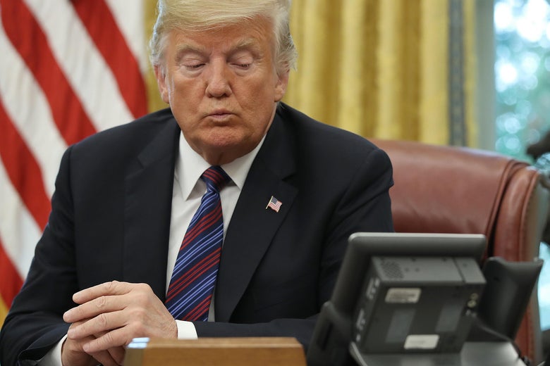 President Trump looks at a telephone on his desk in the Oval Office of the White House.