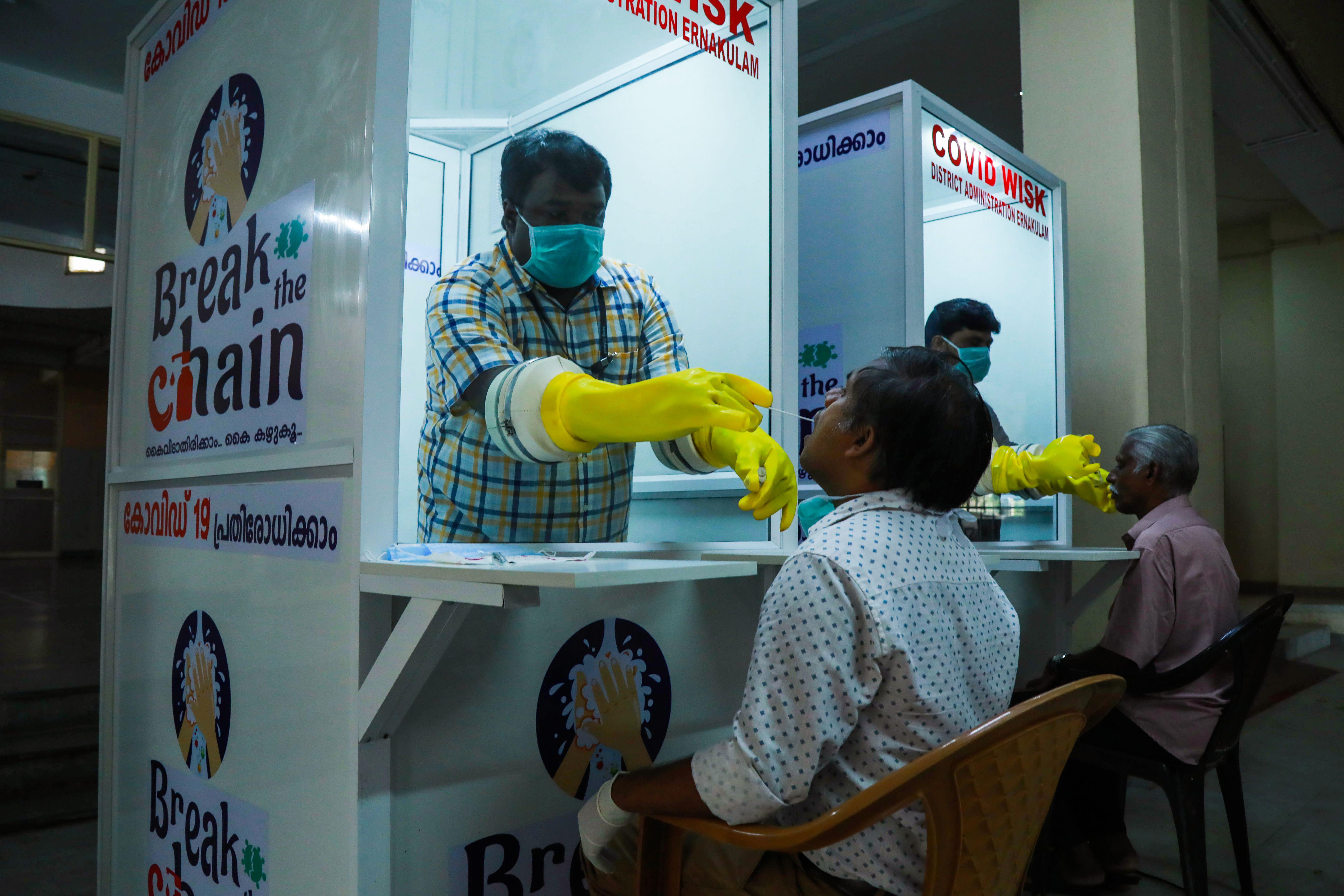 Two kiosks bearing signs that say "Break the Chain." In each kiosk, a medical professional takes a swab sample from a seated person's nose.