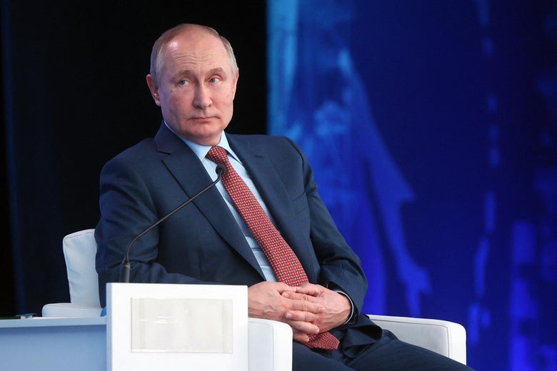 Putin sitting on a stage and leaning nonchalantly on one arm of his chair