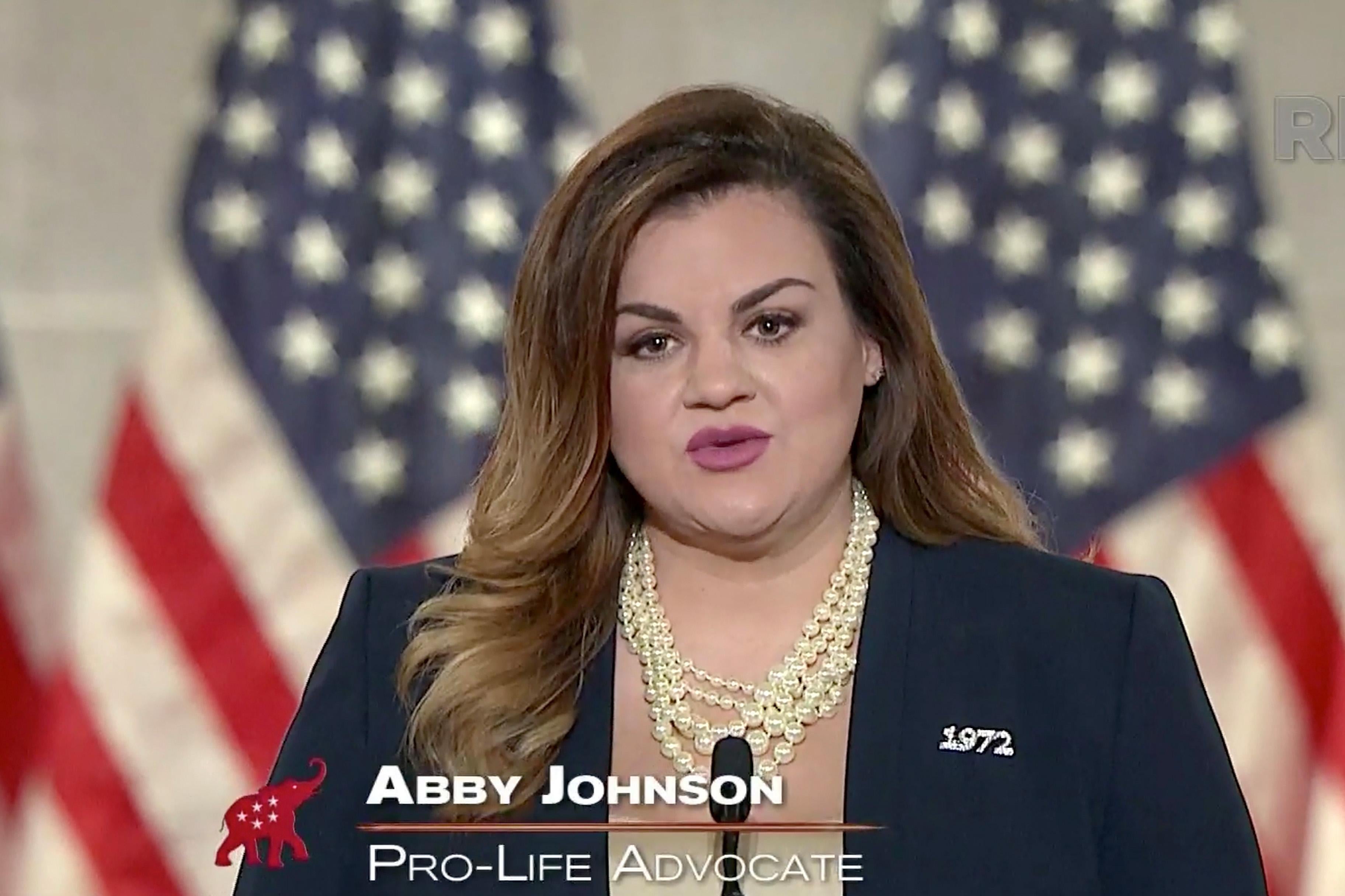 Abby Johnson speaks at a podium, with American flags in the background