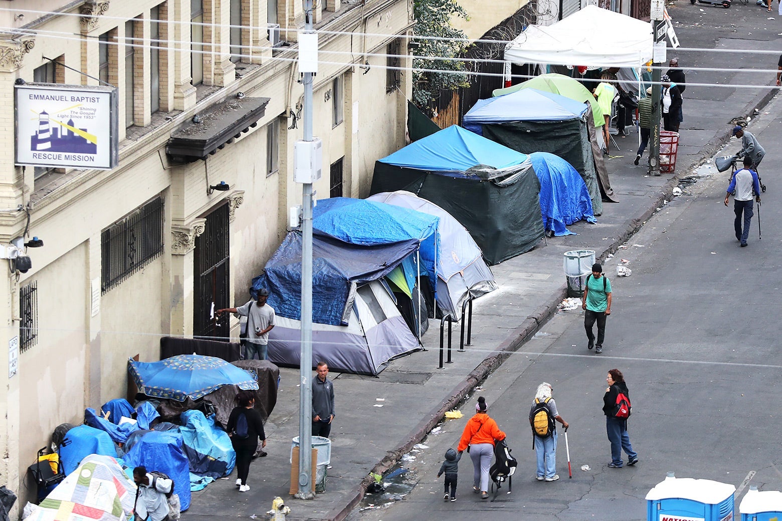 People walk next to a row of tents on Skid Row.