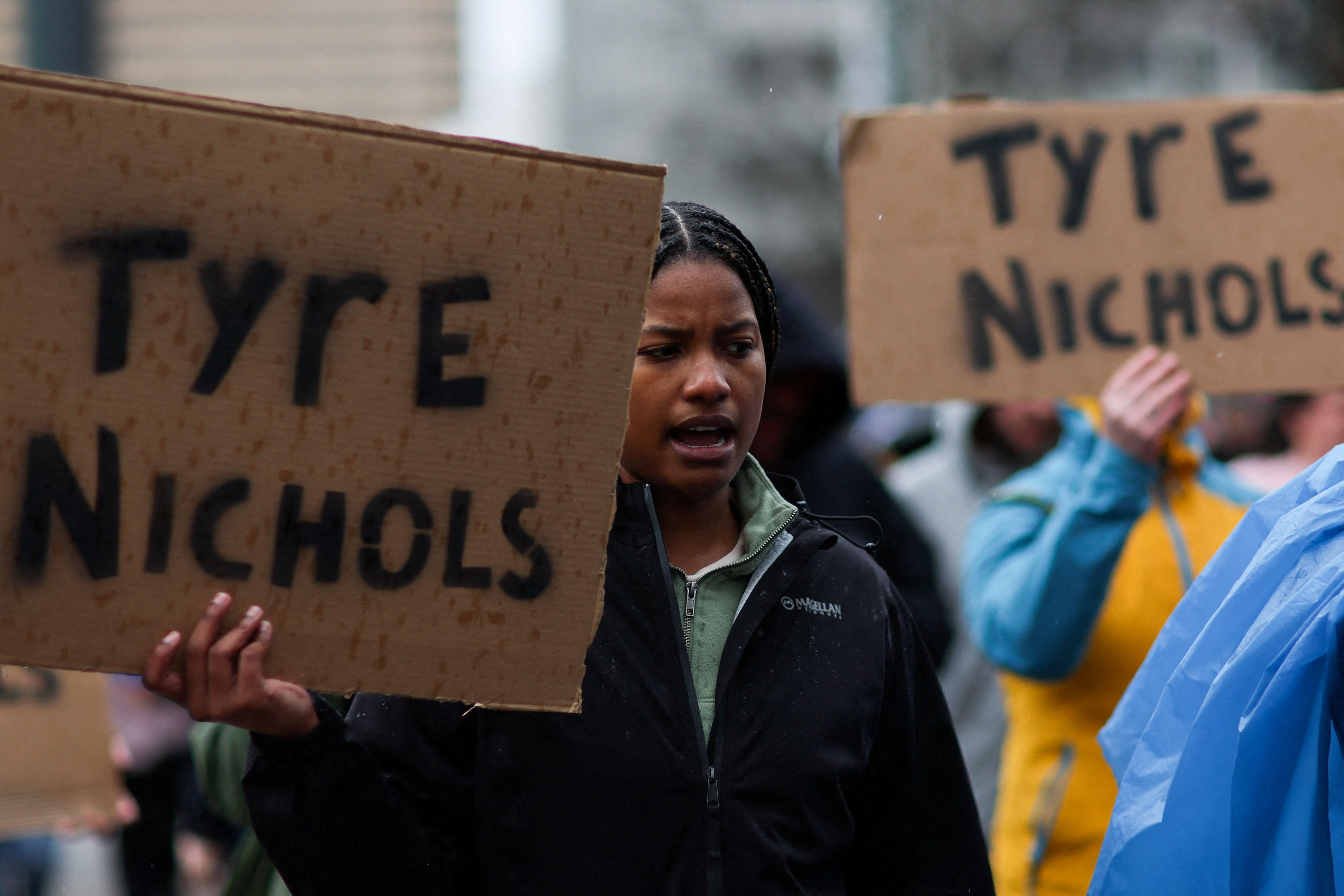A woman holds up a cardboard sign that says TYRE NICHOLS.