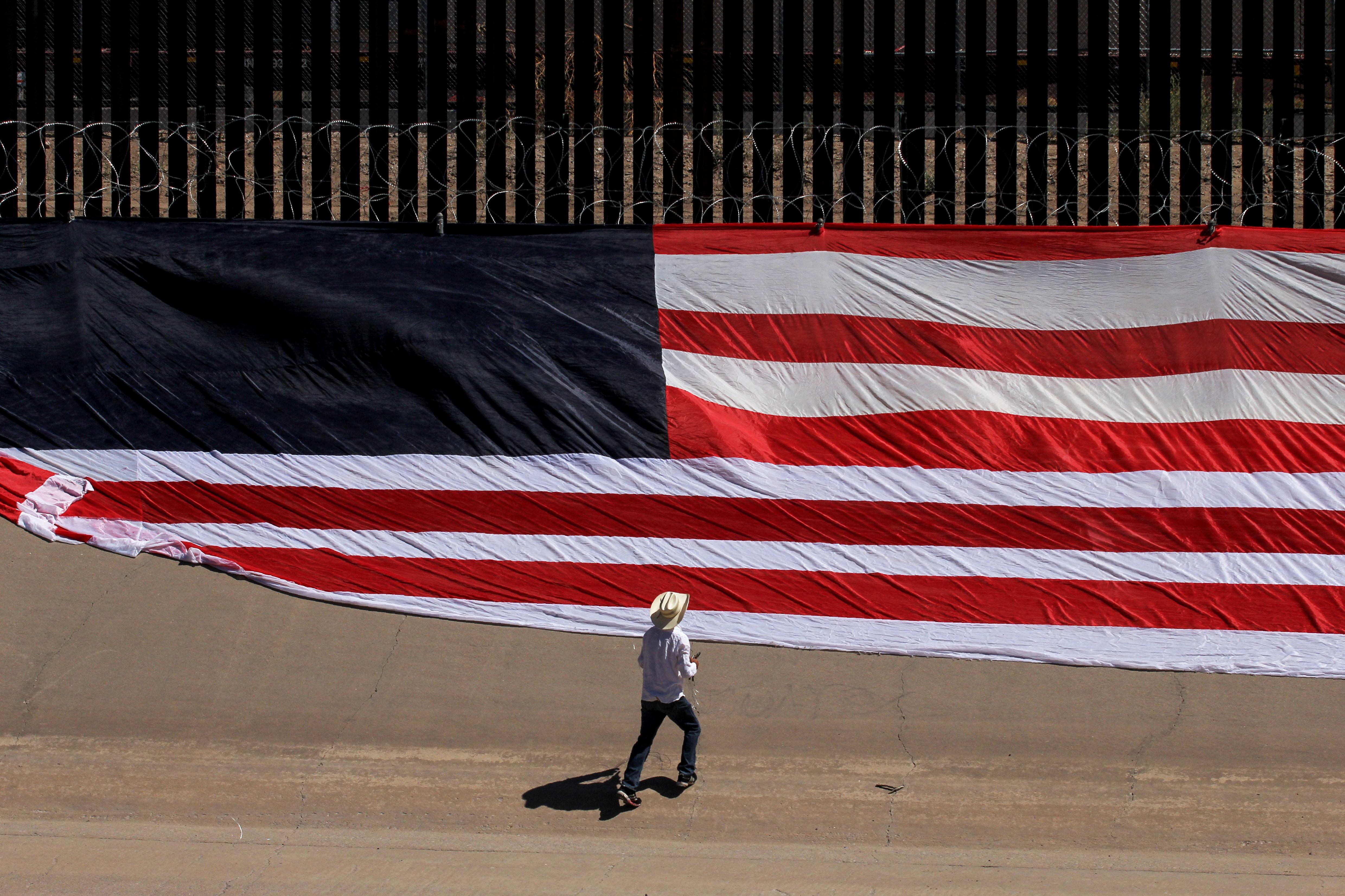 Mexican US resident Roberto Márquez, places a United States national flag on the border wall next to Rio Grande river to demonstrate against the immigration policies of Donald Trump in the border between El Paso and Ciudad Juarez, Mexico, on June 6, 2019.
