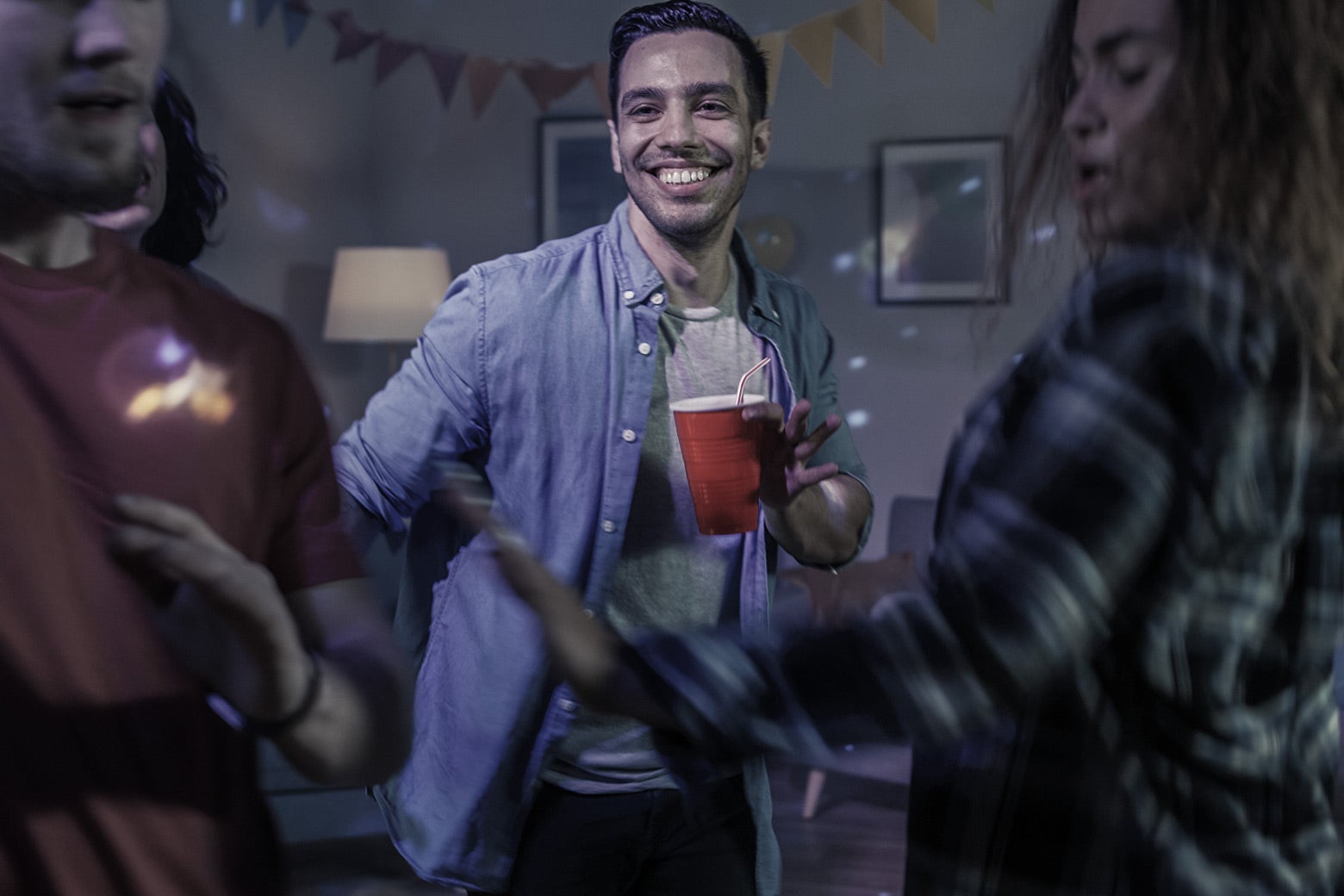 Two men and a woman dance at a party while holding red cups. 