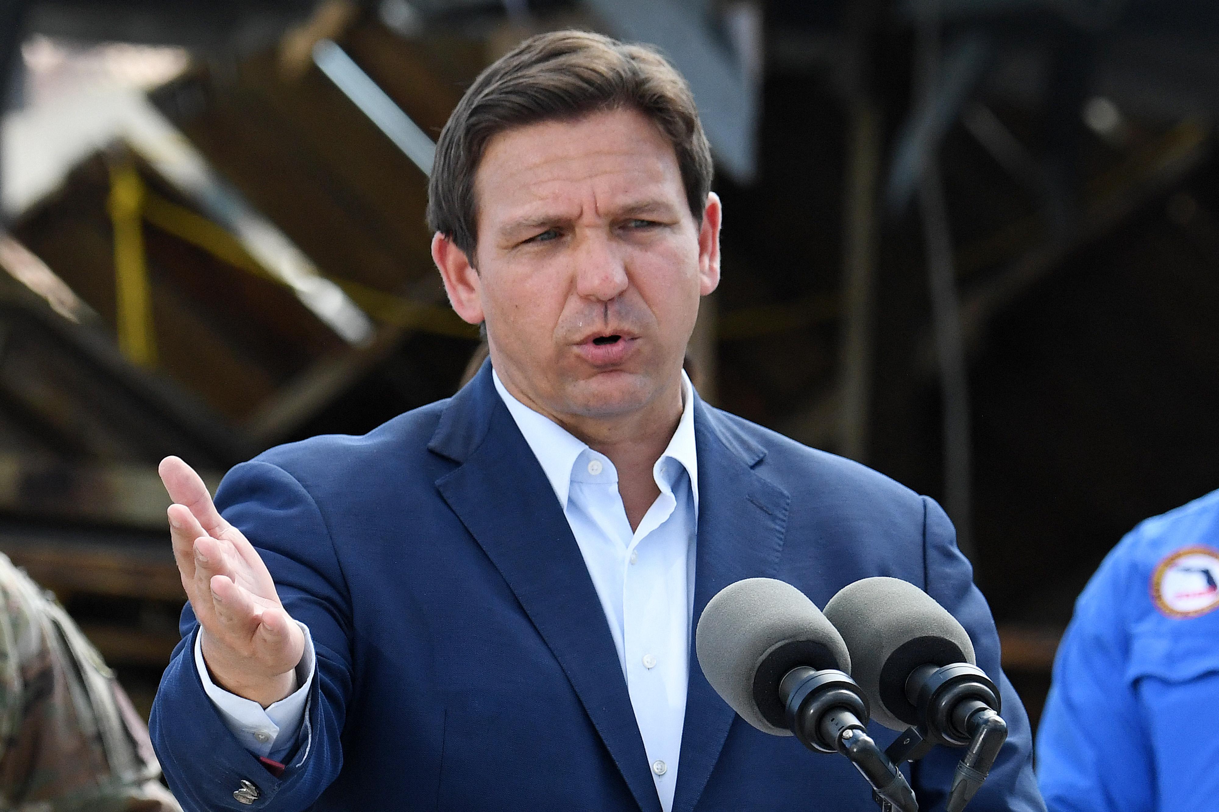 DeSantis gestures with his right hand similar to Donald Trump, wears a suit but no tie.