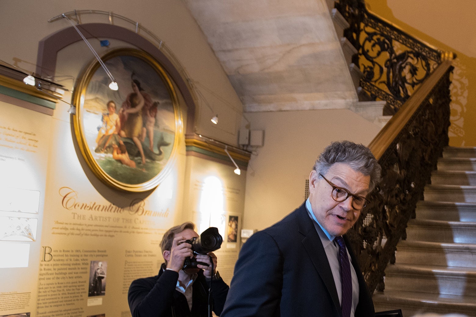 Franken standing next to a staircase in the Capitol as a photographer takes his picture.