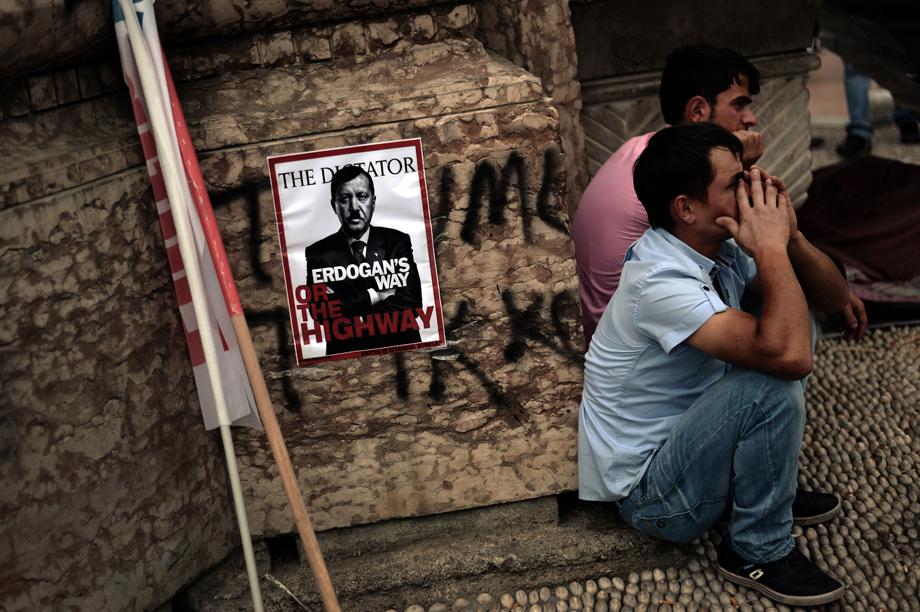 People sit near a poster portraying Turkey's Prime Minister Tayip Erdogan as Hitler in Istanbul on June 5, 2013.