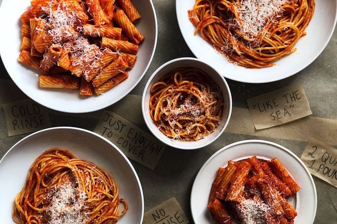 Five white bowls of different kinds of pasta with red sauce, each garnished with cheese shavings.