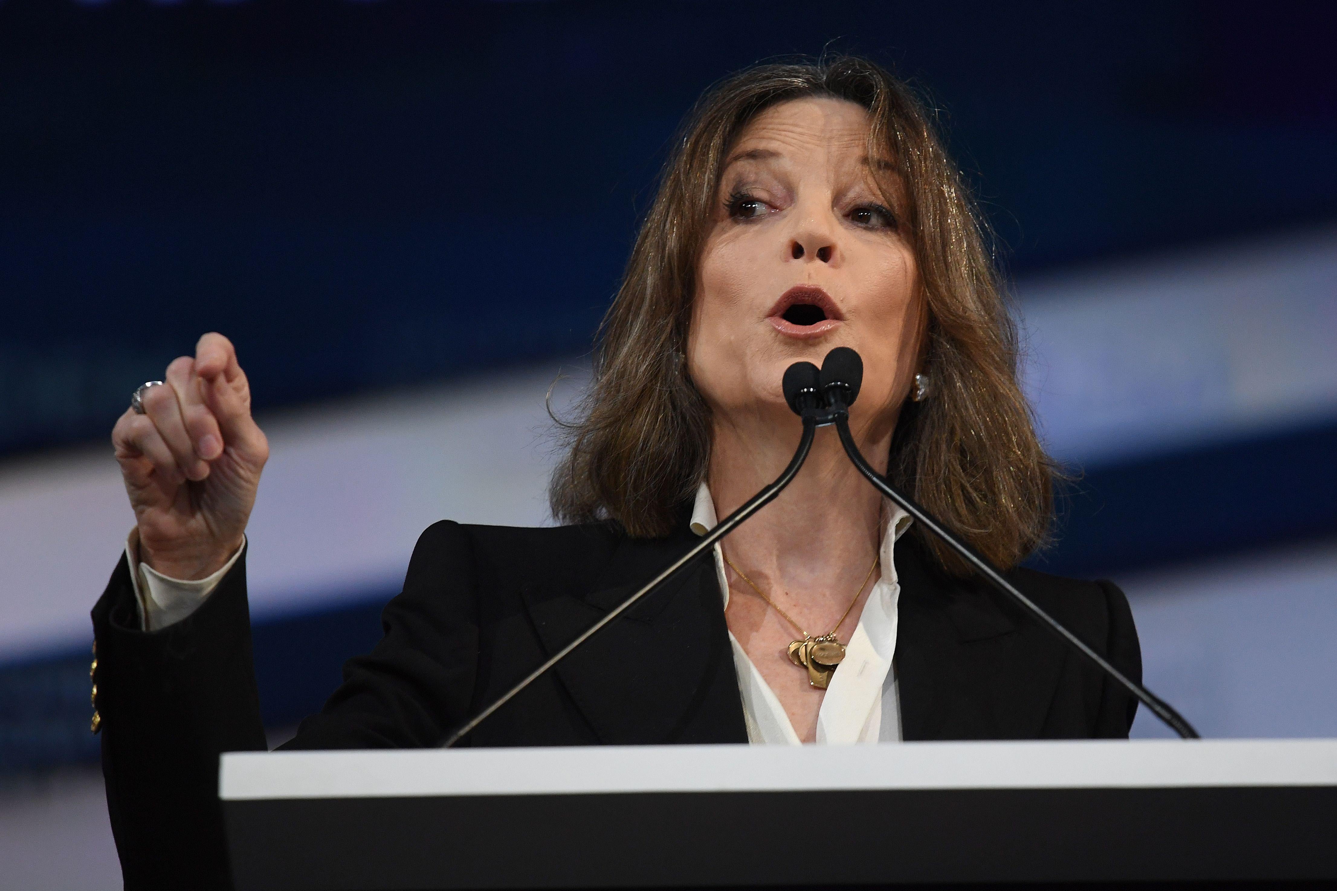 Marianne Williamson gesturing as she speaks in front of a podium.