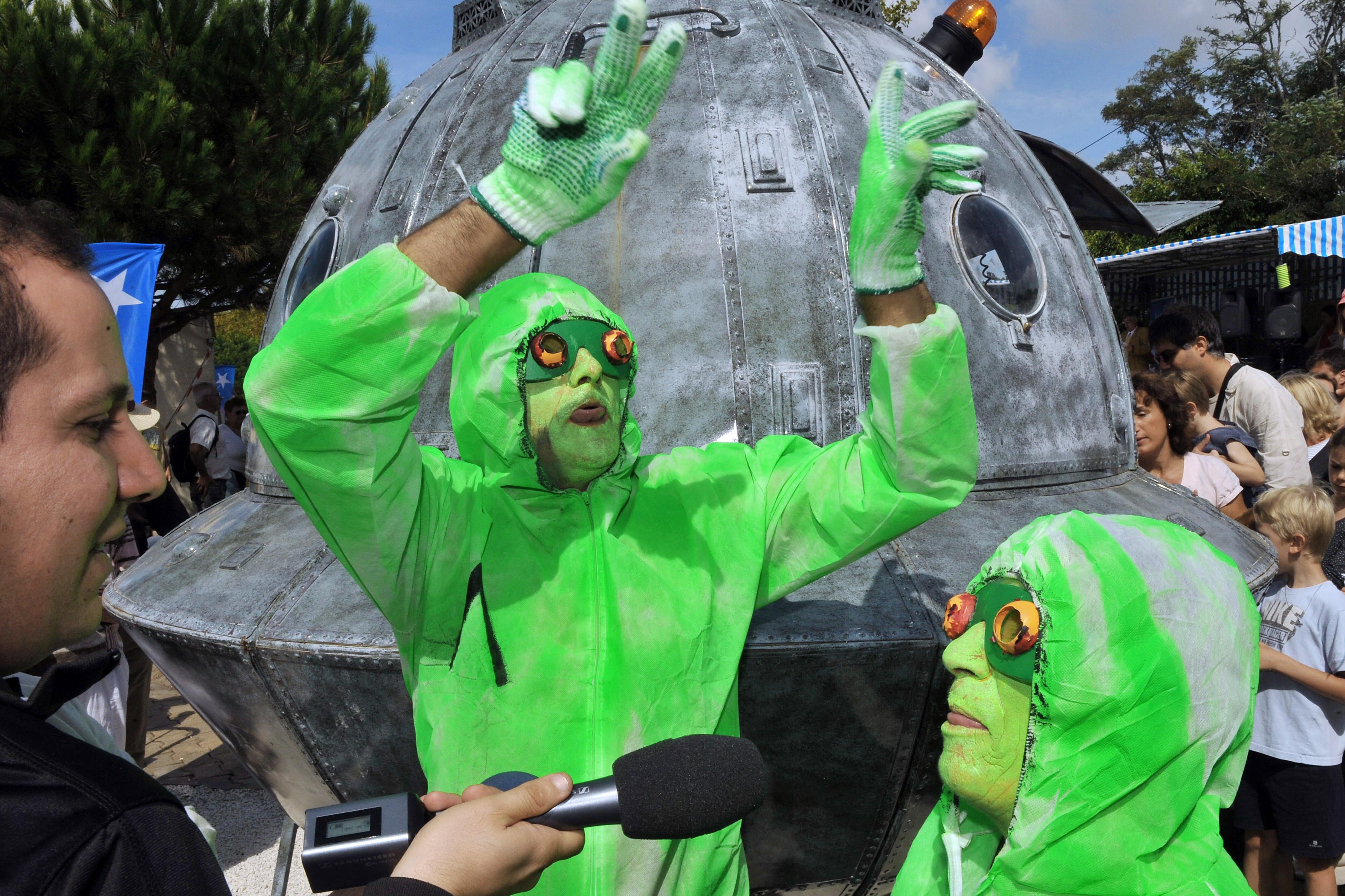 Two people in green outfits and face paint in front of a fake flying saucer