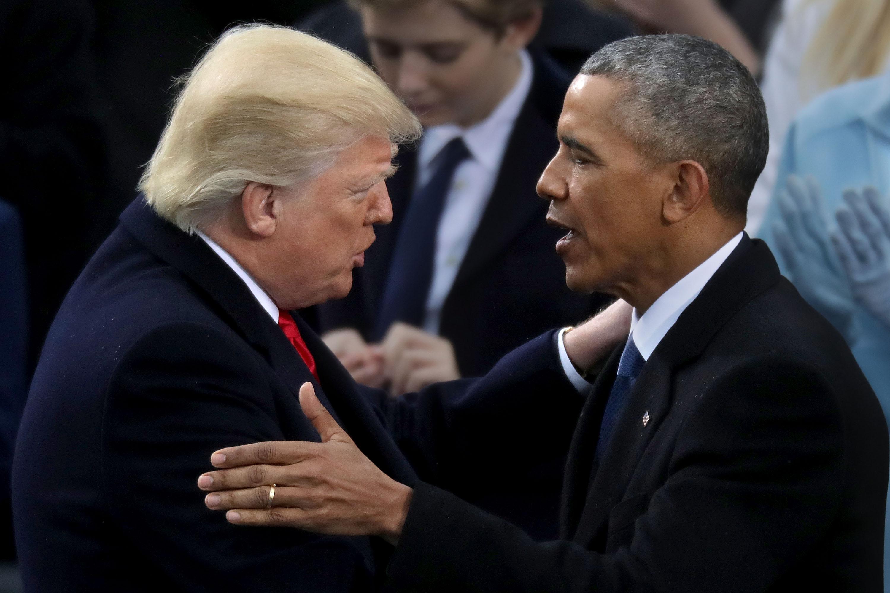 Trump and Obama touch each other's shoulders while speaking face to face.