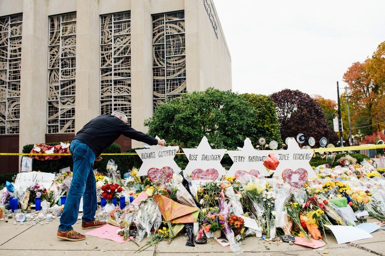 A man adjusts a marker for a shooting victim at the memorial outside Tree of Life synagogue. The memorial is full of flowers.