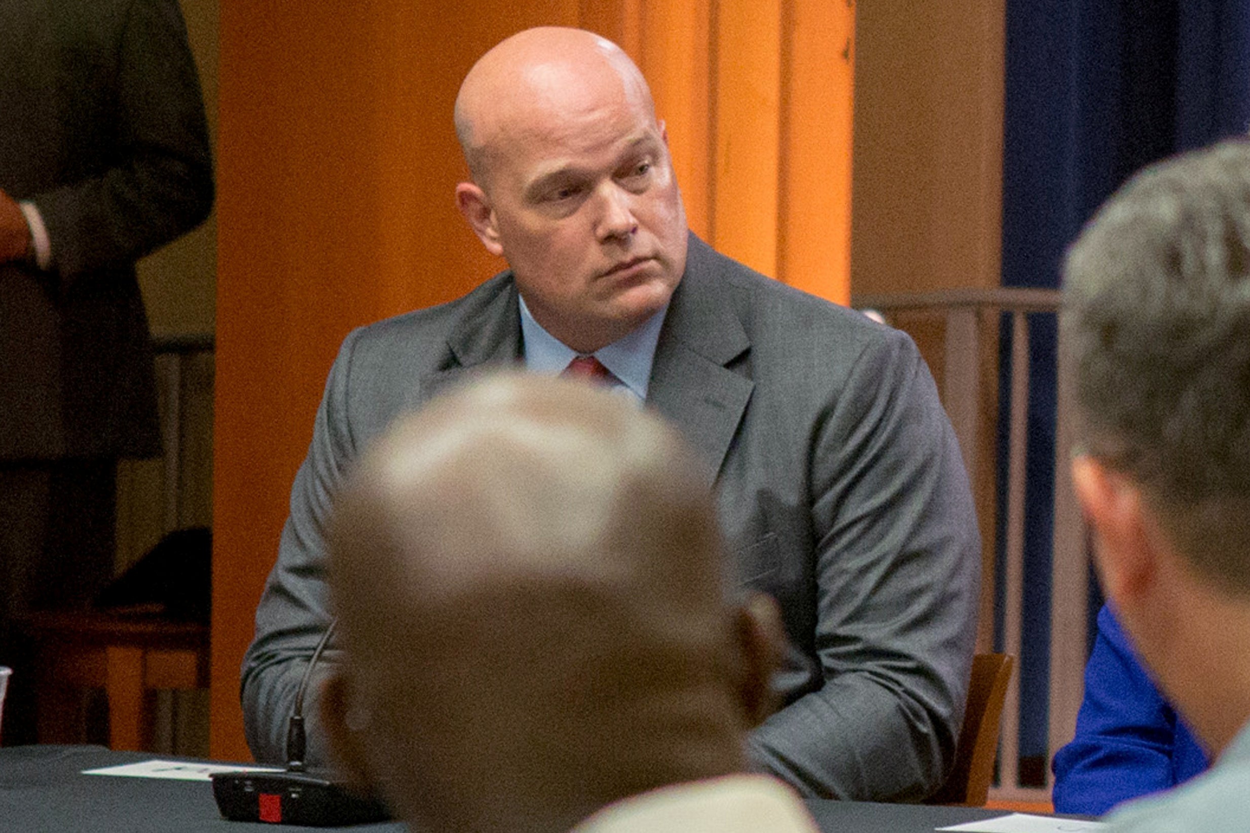 Whitaker sitting at a table. He's bald. The view of him is partially blocked by a different bald guy.