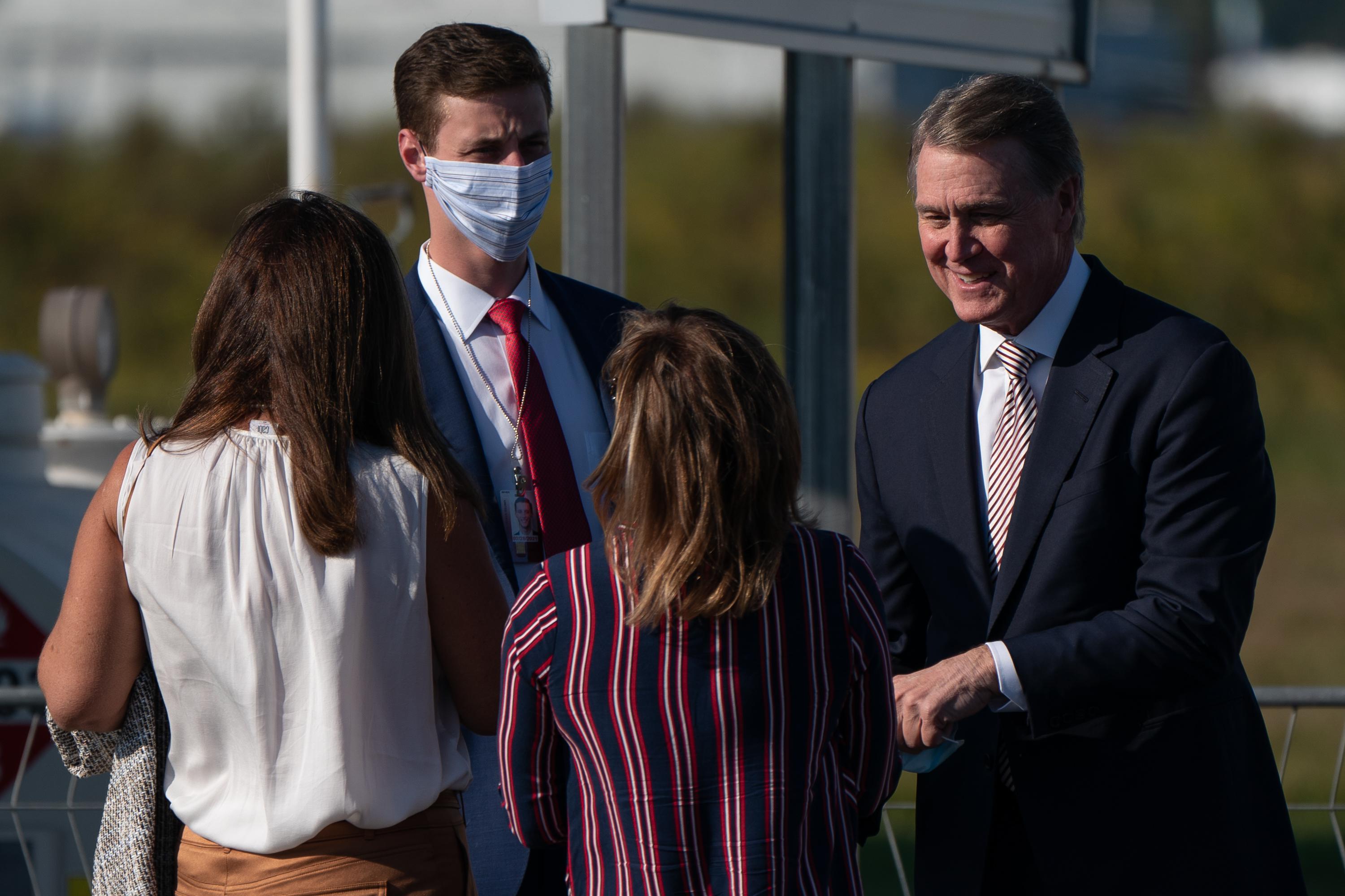 A man without a mask talks with two women while a man stands at his side in a face mask.