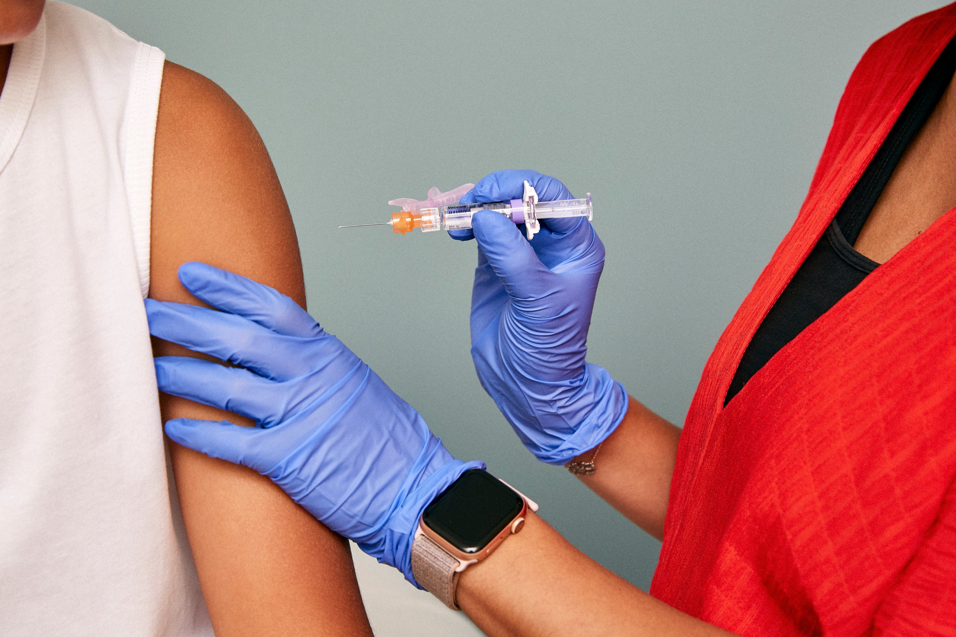 A medical professional wearing gloves holds a syringe up to a patient's upper arm