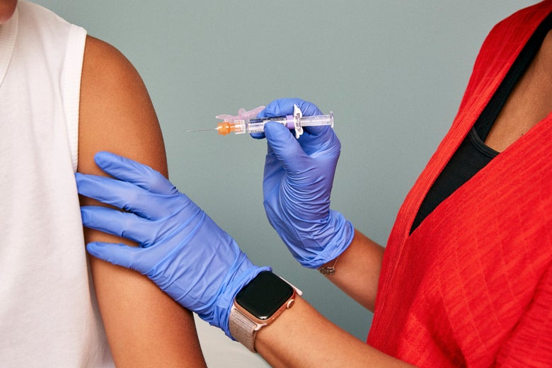 A medical professional wearing gloves holds a syringe up to a patient's upper arm
