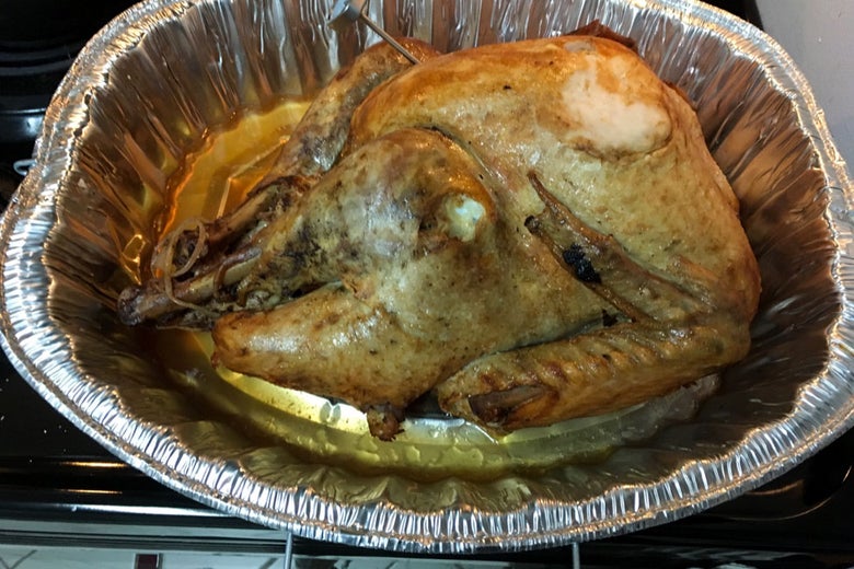 A more cooked but still yellowish turkey in a foil roasting pan.