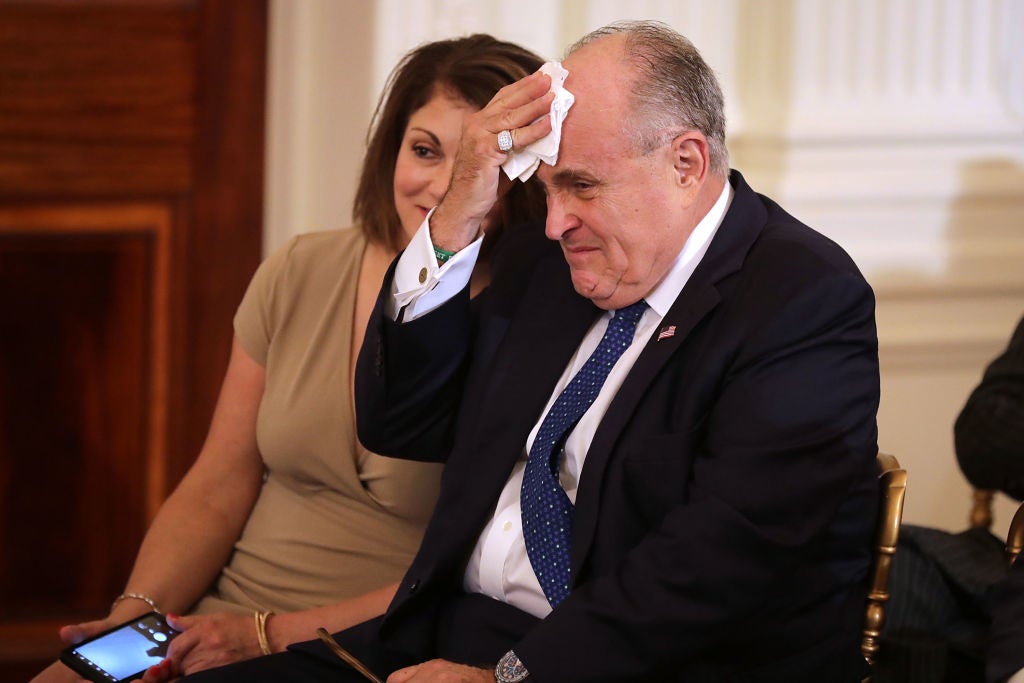 Giuliani, seated in a chair, wipes his head with a handkerchief.