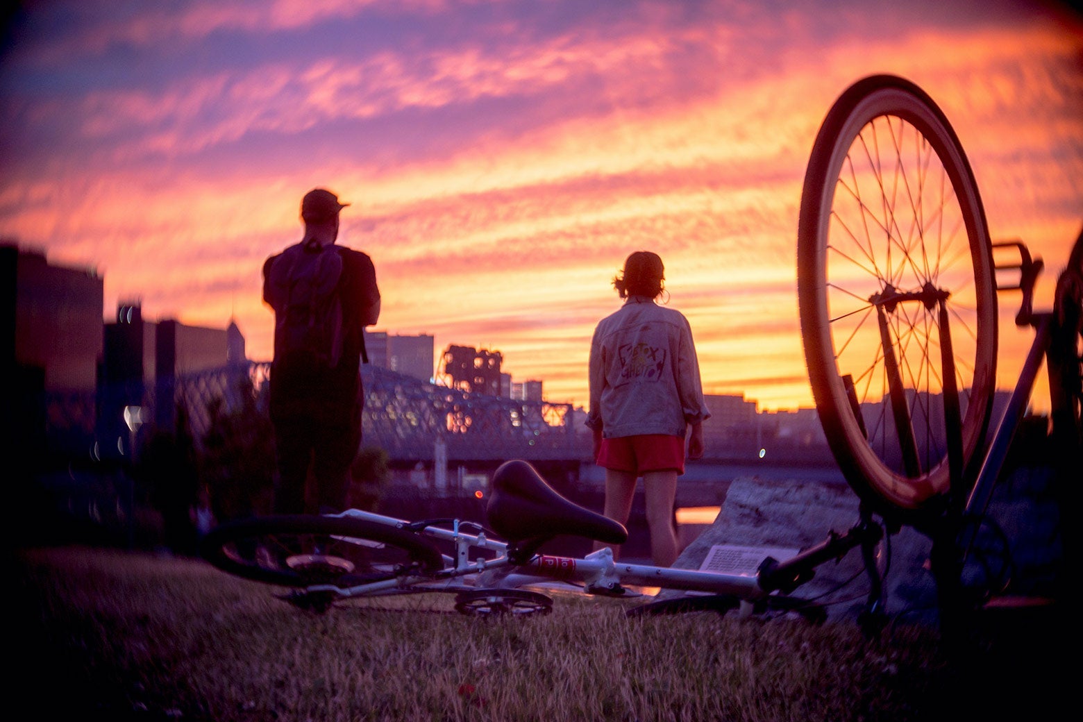 A bicycle is seen lying on the ground. Two people stand in front of it.