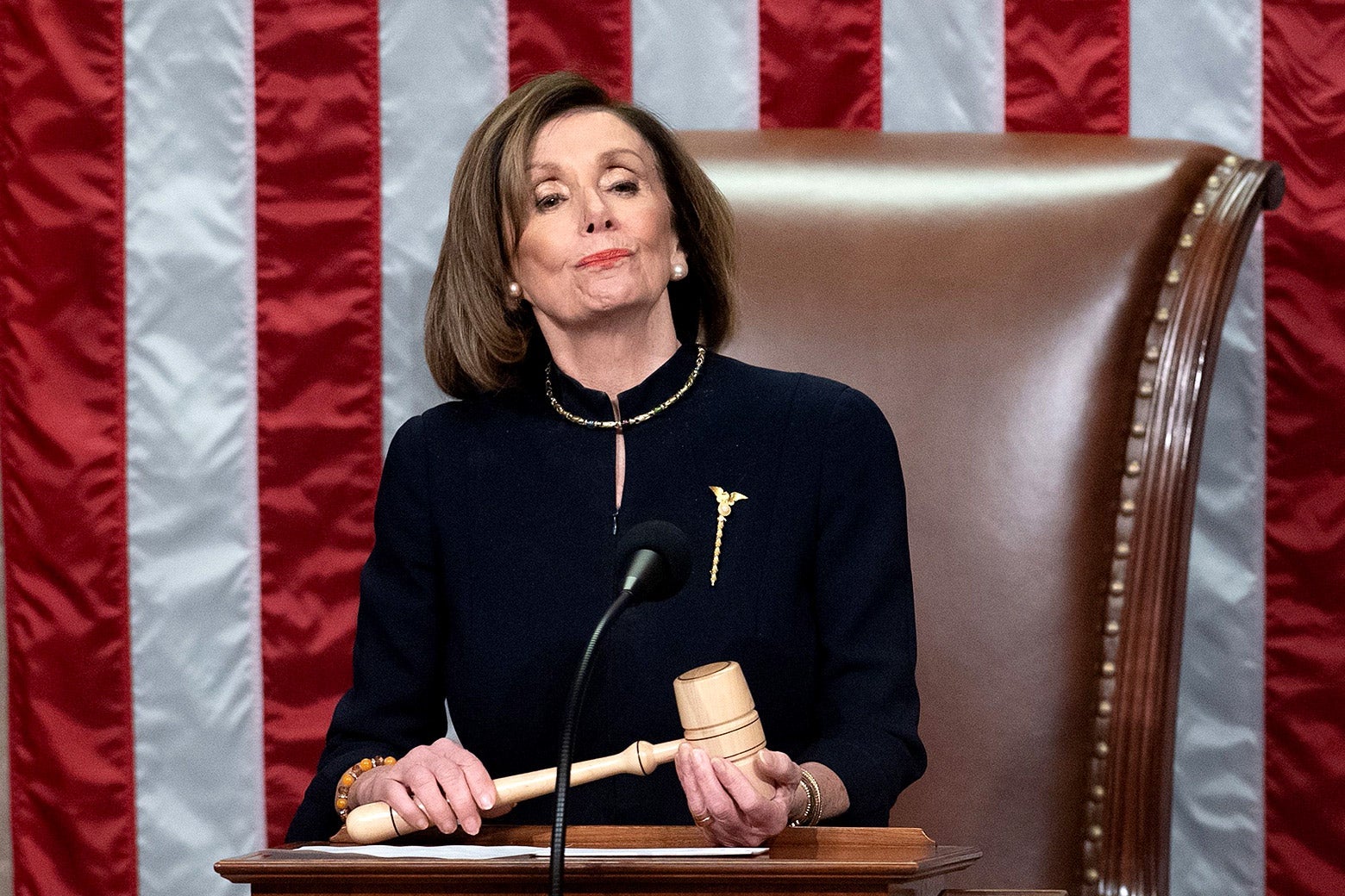 Nancy Pelosi holds a gavel while standing at a podium in front of an American flag.