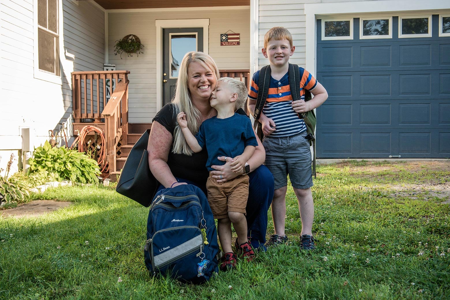 Heather smiles with her two boys in a yard outside a house