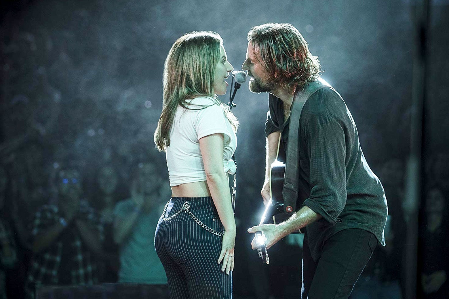 In a scene from A Star Is Born, Lady Gaga and Bradley Cooper sing into a mic onstage.