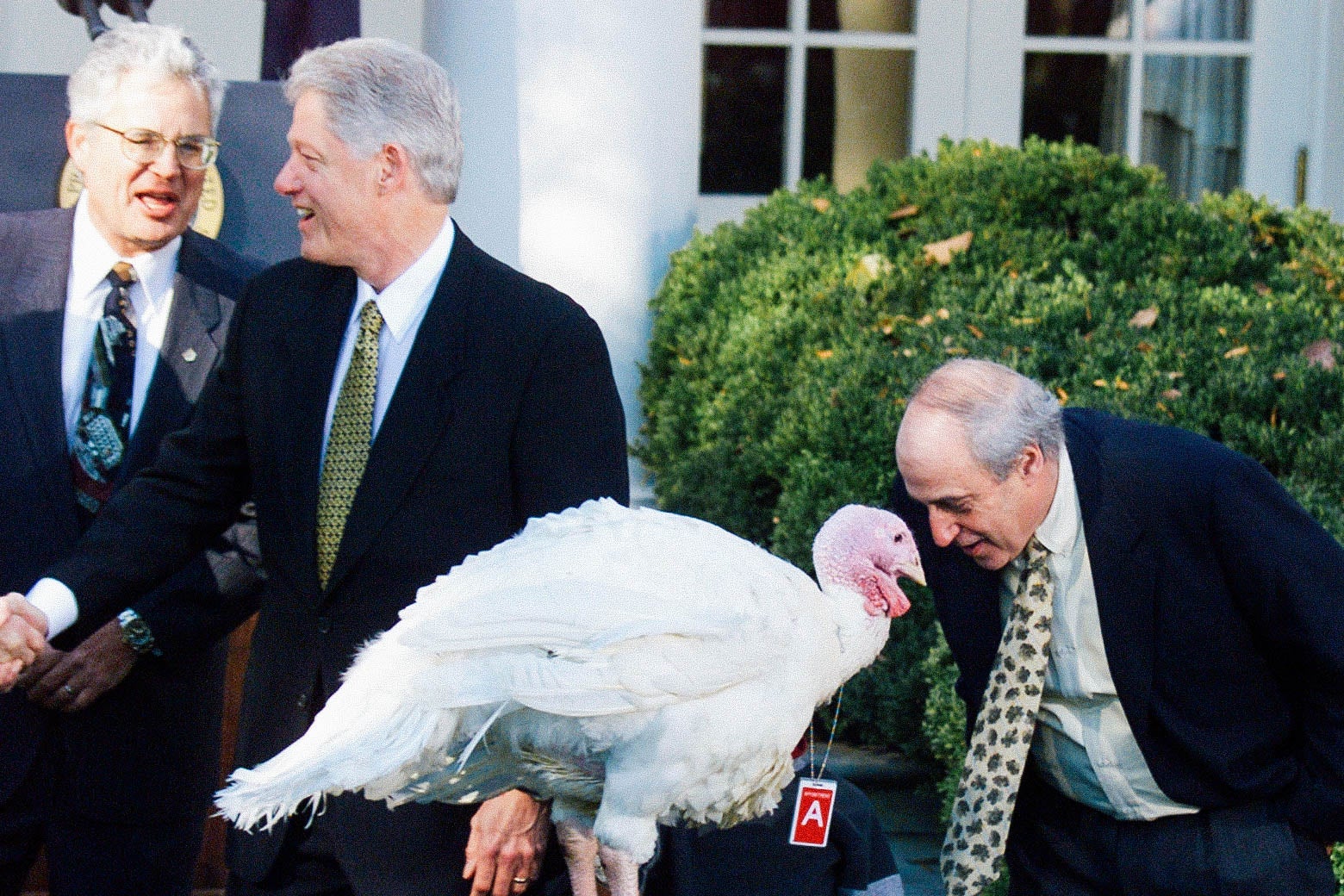A man in a suit bends down to put his face up to a turkey. Bill Clinton stands next to them.