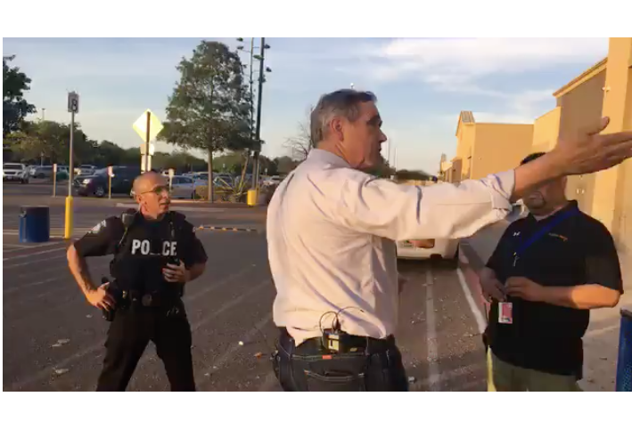 Merkley gestures toward the facility as a police officer looks on.