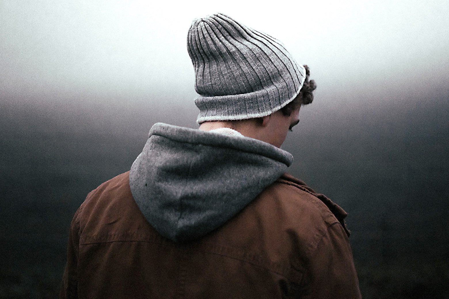 A teenaged boy with a coat and knit hat facing away from the camera.