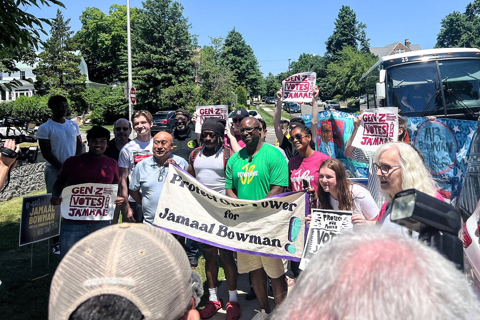 Bowman at an event, standing with a group holding signs that say "Protect Our Power for Jamaal Bowman" and "Gen Z Votes For Jamaal."