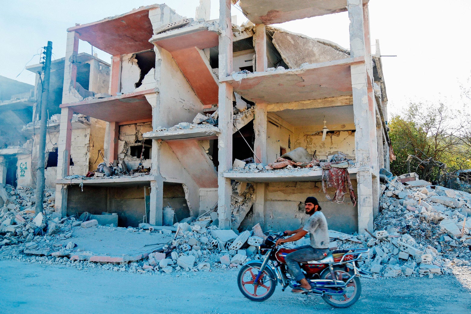 A Syrian man rides a motorcycle past a destroyed building.