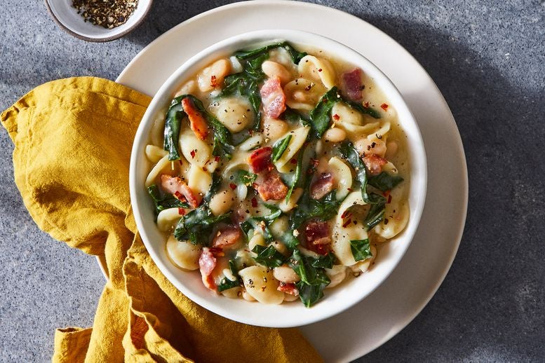 Bowl of orecchiette with bacon, collard greens, and cannellini beans on a plate