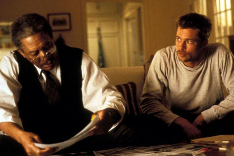 Morgan Freeman and Brad Pitt sit on a couch in a living room looking at photos and documents.